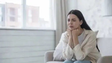 Žena sedí na gauči s rukama pod bradou v úzkosti.