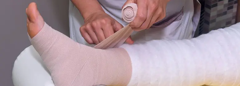 Zdravotník obaluje oteklou nohu elastickým obvazem.