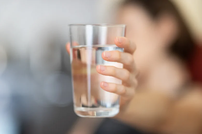 Ruka drží sklenici vody jako symbol hydratace těla.