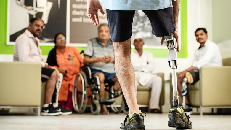 Osoba s protézou nohy stojí před skupinou lidí v rehabilitačním prostředí.