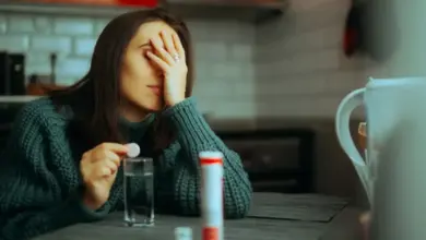 Žena sedí u stolu s tabletami a sklenicí vody.