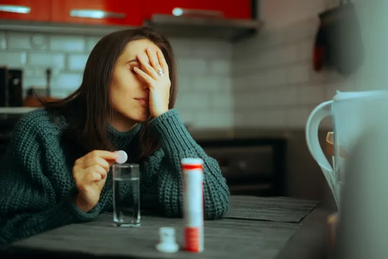 Žena sedí u stolu s tabletami a sklenicí vody.