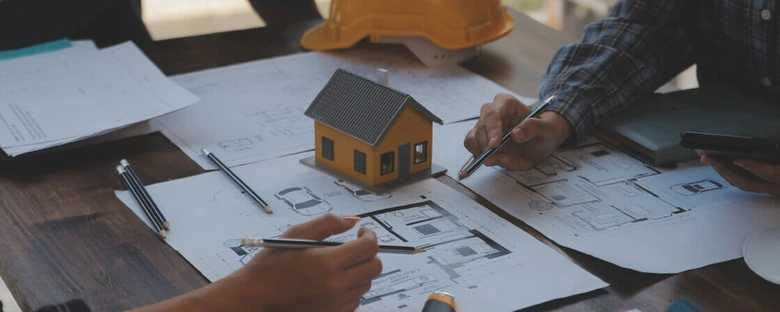 Architektonické plány s modelem domu na stolu pro projektovou dokumentaci.