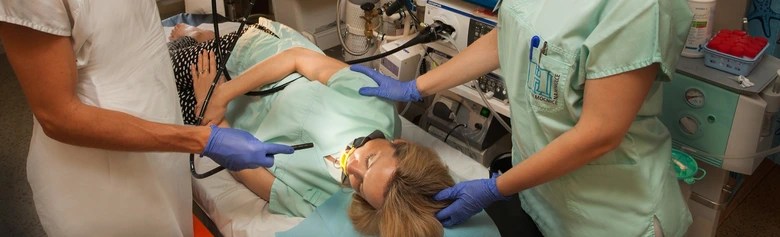 Pacientka leží na stole při gastroskopii s lékařskými pracovníky.