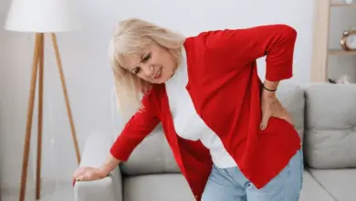 Žena drží si záda v bolesti na pohovce.