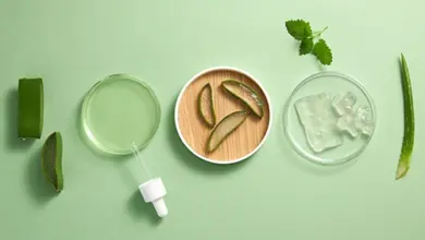 Suroviny aloe vera s listy, gelem v miskách a pipetou na zeleném pozadí.