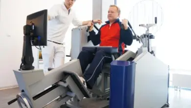 Muž cvičí na rehabilitačním stroji pod dohledem fyzioterapeuta.