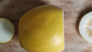 Žlutý oloupaný pomelo na dřevěném prknu s odříznutými kousky.