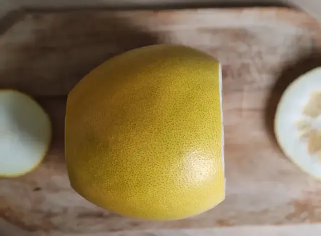 Žlutý oloupaný pomelo na dřevěném prknu s odříznutými kousky.