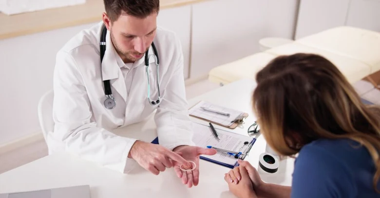 Lékař ukazuje pacientce hormonální vaginální kroužek při vyšetření.