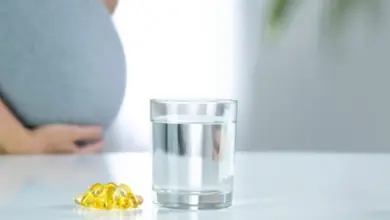 Těhotná žena s vitamíny a sklenicí vody na stole.