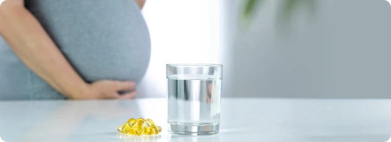 Těhotná žena s vitamíny a sklenicí vody na stole.