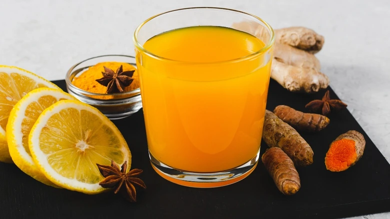 Sklenice s džusem z kurkumy a citronu se suroviny kolem.