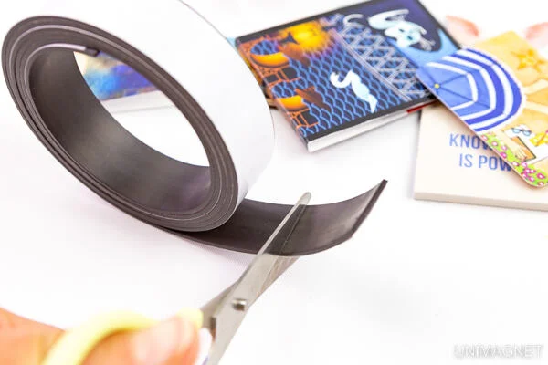 Ruční nůžky řezou samolepicí magnetickou pásku na bílém pozadí.