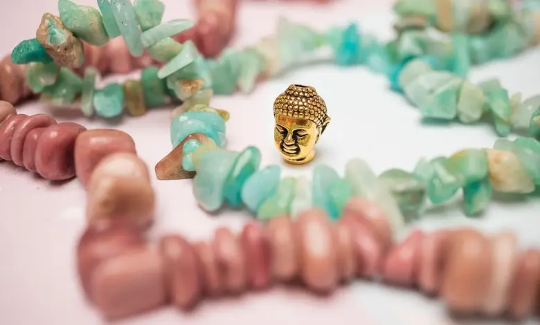 Zlatá Buddha mezi růžovými kameny na bílém pozadí.