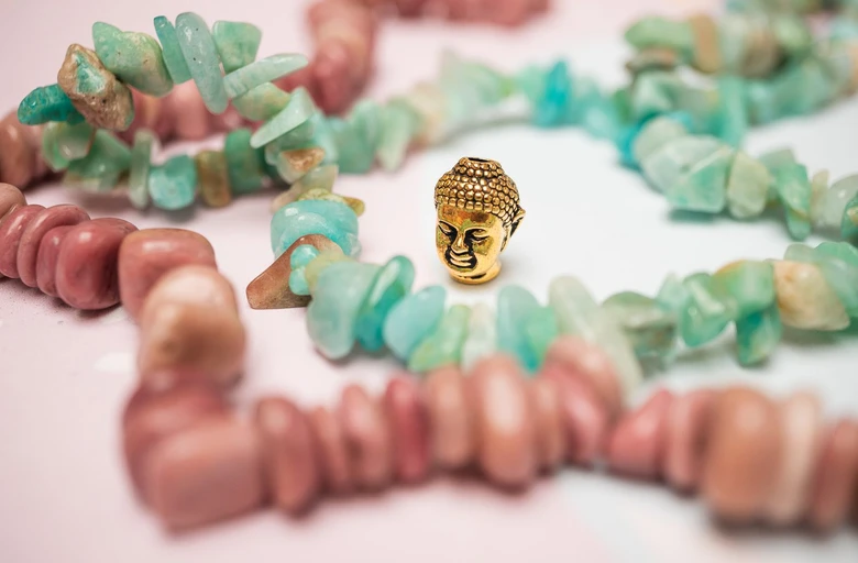 Zlatá Buddha mezi růžovými kameny na bílém pozadí.