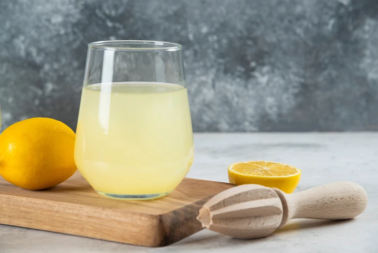 Sklenice čerstvého citronového džusu s citrónem na dřevěné desce.