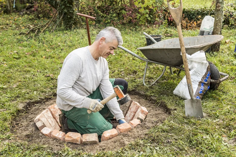 Muž staví venkovní ohniště z cihel v zahradě.